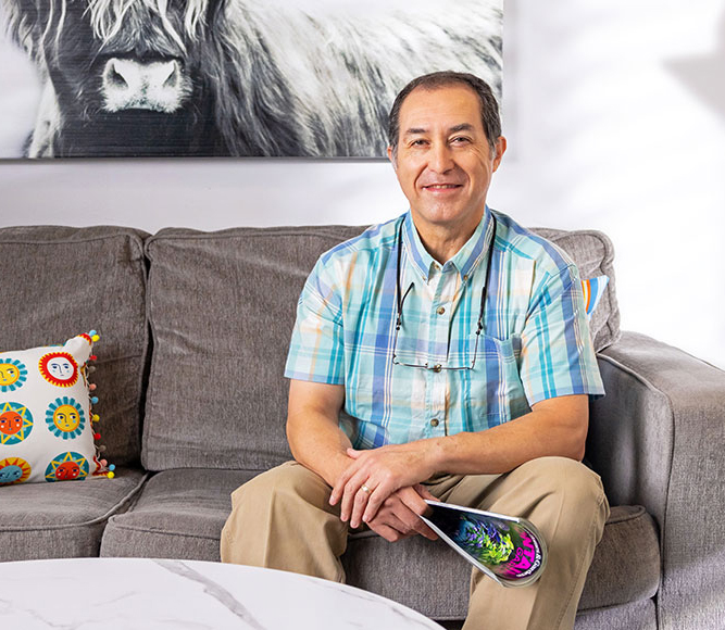 Man sitting on a couch in his apartment smiling and holding a magazine