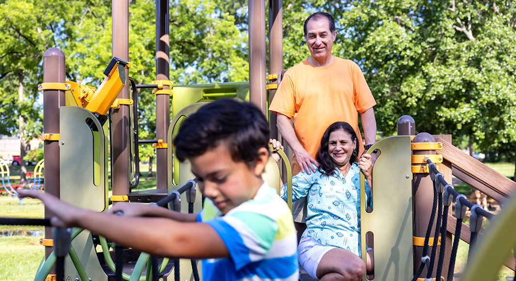 Grandparents playing on a park slide with their grandson
